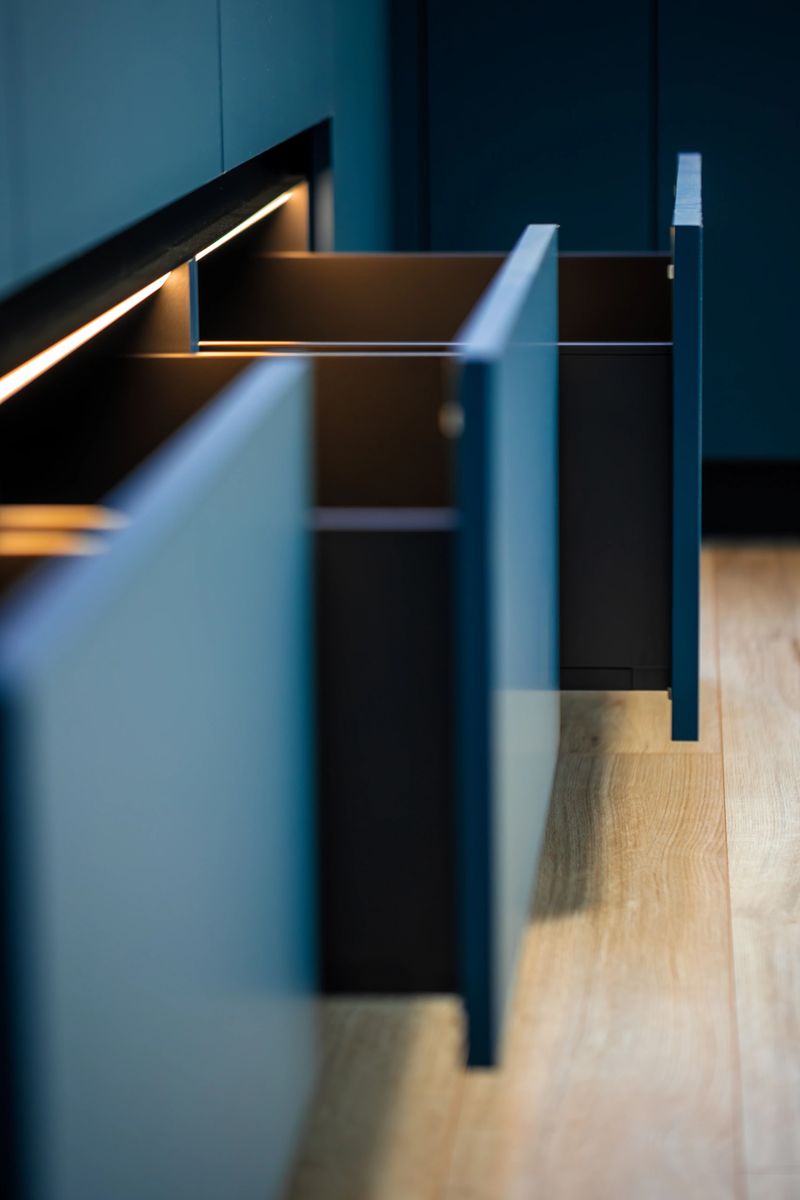 A sequence of open sections with a warm LED line adds depth and flow. Sharp edges and calm tones showcase contemporary kitchen cabinetry.