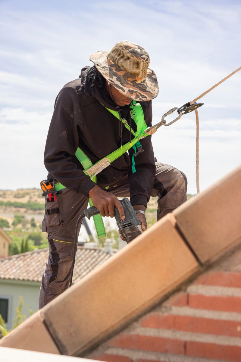 Young african american roofer securing tiles on a rooftop, demonstrating workplace safety