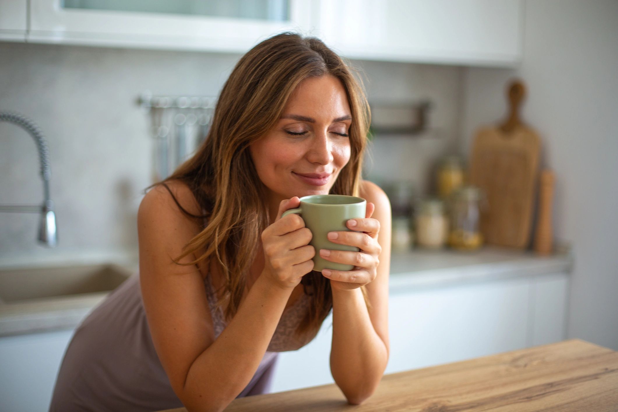 Woman enjoying a warm drink with eyes closed and a smile.