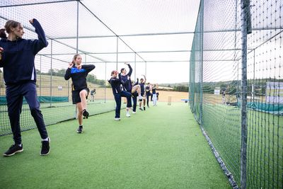 Young athletes practicing pitching drills in a cricket net.