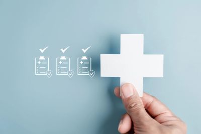 Hand holding a white medical cross with checklist icons.