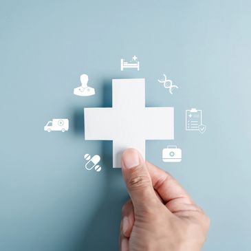 Hand holding a white medical cross with healthcare icons around it on blue background.