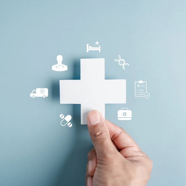 Hand holding a white medical cross with healthcare icons.