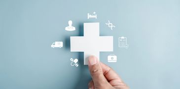 Hand holding a white medical cross with healthcare icons around it.
