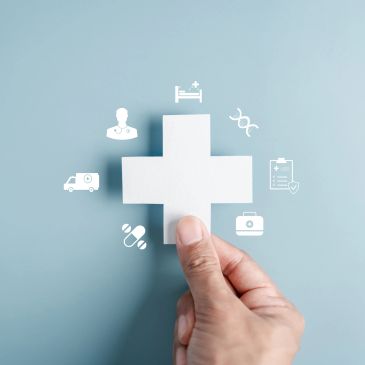 Hand holding a white medical cross with healthcare icons.