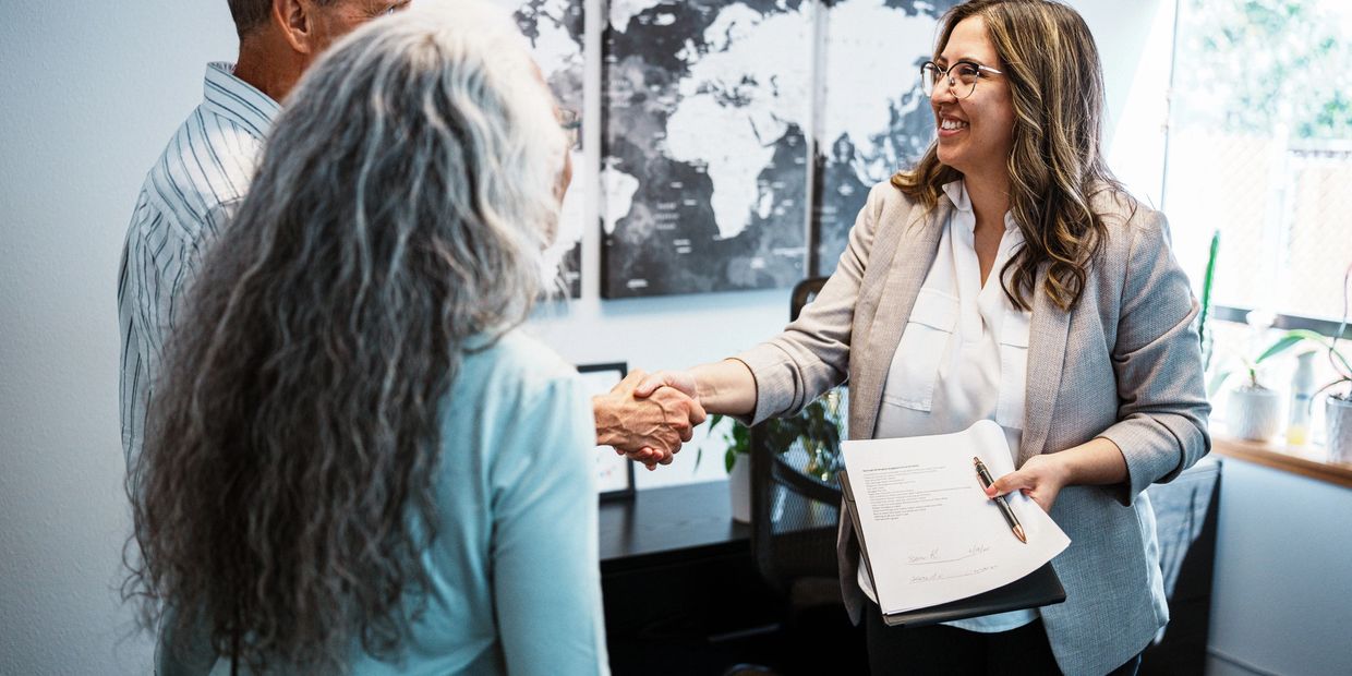 A woman shakes hands with a couple in a professional office setting.
