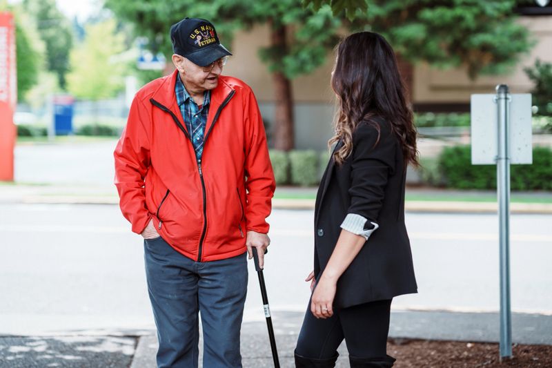 A senior veteran stops to talk with a friendly credit union employee on the sidewalk outside a credit union on a sunny afternoon.