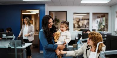 Woman holding child with teddy bear in an office.