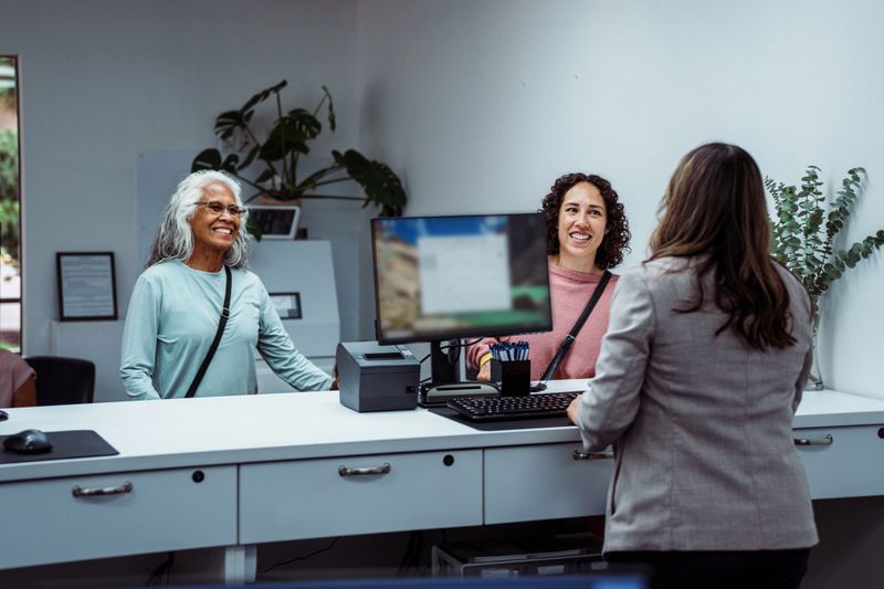 A senior woman of Hawaiian and Chinese descent and her Eurasian adult daughter cheerfully talk with a female customer service representative at the bank counter of a local credit union.