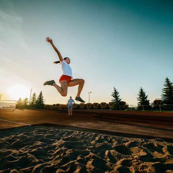 Athlete jumps during long jump at sunset on outdoor track field.