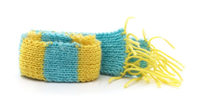 Handmade knitted scarf in yellow and blue colors isolated on white background, warm winter clothing accessory, wool fashion detail and cozy handmade craft.