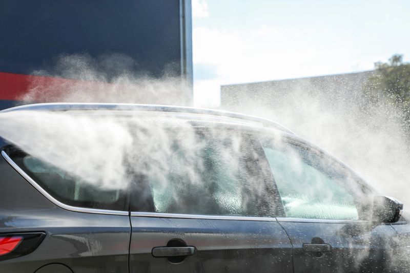 Car being thoroughly cleaned with a powerful high-pressure jet under radiant sunlight, highlighting gleaming surfaces and professional car care (part of the “at the car wash” series).