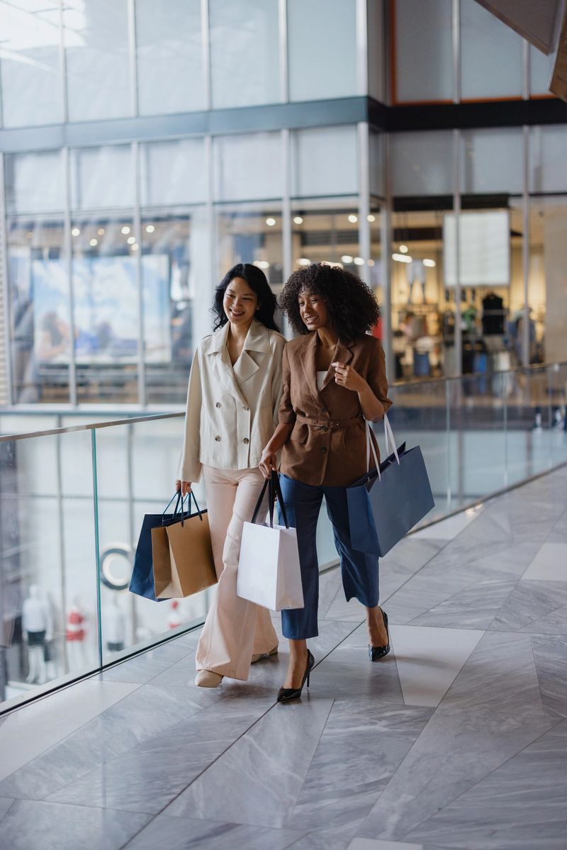 Two joyful female friends enjoying a vibrant shopping spree while walking through a modern mall, carrying stylish bags and sharing laughter
