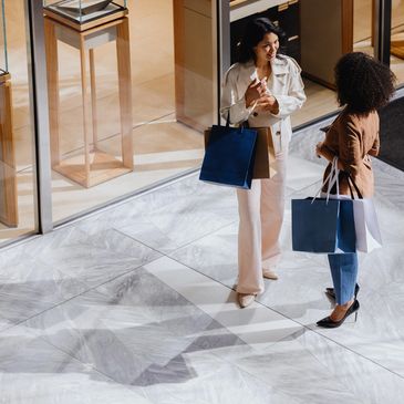 Two women chatting happily with shopping bags outside a store.