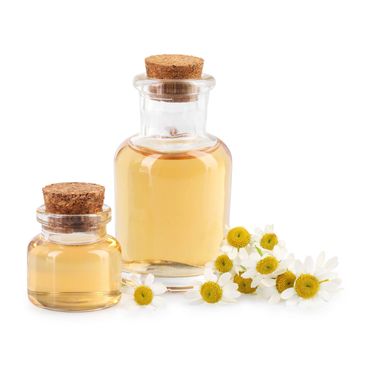 Two glass bottles with corks filled with chamomile oil and fresh chamomile flowers.