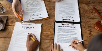 People reviewing and signing contracts on a wooden table.