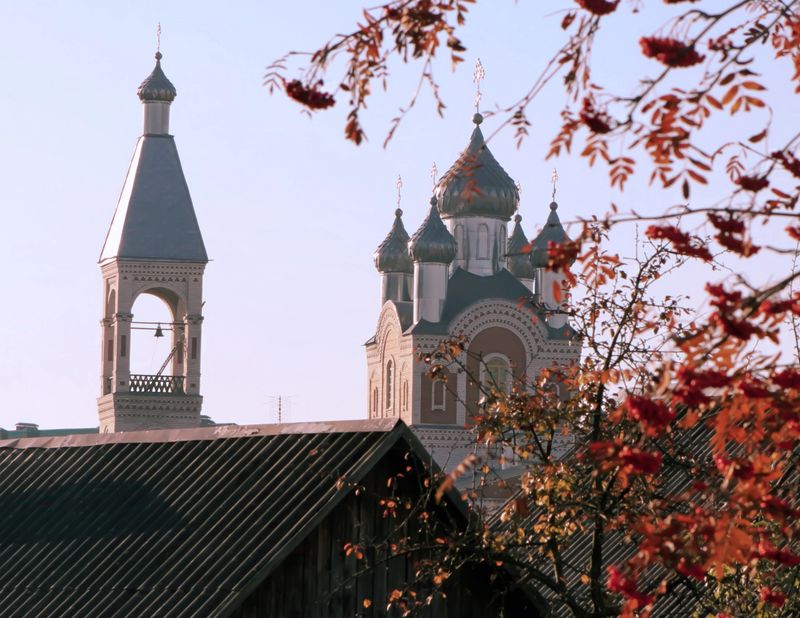 A historic church with ornate details stands tall amidst colorful autumn leaves in a serene small town setting, showcasing seasonal beauty.