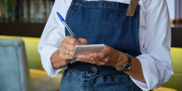 Waiter in blue apron taking order with pen and notepad.