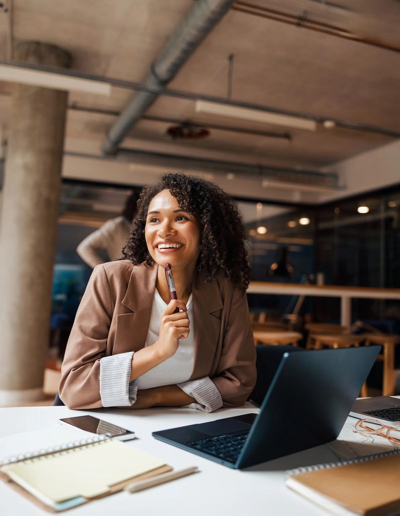 A professional woman is thoughtfully considering ideas in a stylish office while working on her laptop