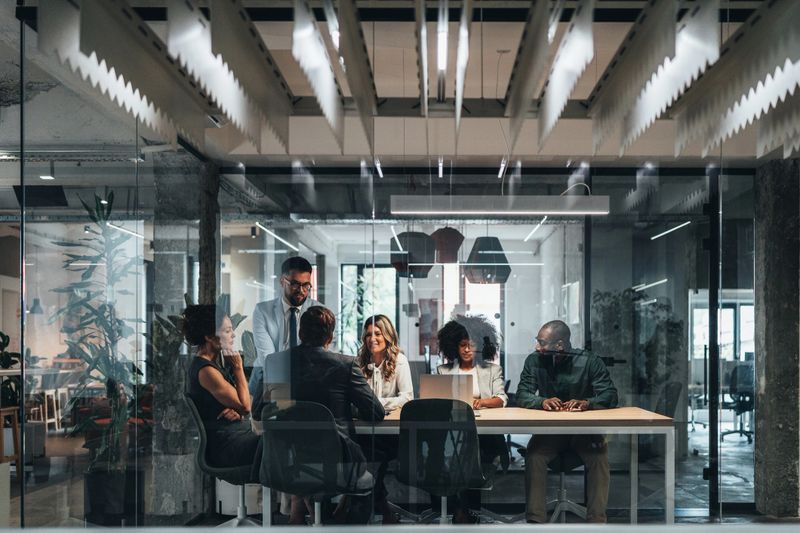 A diverse team of professionals engaged in a collaborative business meeting inside a modern glass-walled conference room