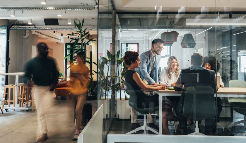 A diverse team of professionals engaged in a collaborative business meeting inside a modern glass-walled conference room