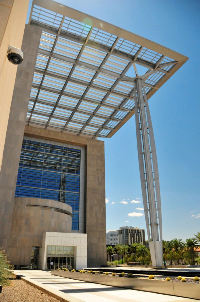 Las Vegas, Clark County, Nevada, USA: the Lloyd D. George United States Courthouse, located on Las Vegas Boulevard South between Bridger and Clark Avenues, serves as a federal judicial facility named in honor of Lloyd Dee George, a longtime U.S. District Judge for the District of Nevada, recognized for his judicial contributions when Congress approved the naming in 1998. Completed in 2000, the eight-story, approximately 456,000-square-foot structure was designed by Mehrdad Yazdani of Dworsky Associates (now Cannon Design) under the U.S. General Services Administration's Design Excellence Program, featuring an L-shaped configuration that includes a raised plaza with a broad staircase, water pool, trees, and a large trellis-canopy supported by an articulated column. The architecture employs a steel frame with varied facades—horizontal glass bands and limestone on the public-facing side for transparency, smaller windows in metal panels on the office side, and precast concrete panels for the courtrooms—incorporating materials such as limestone, metal, granite, and terrazzo in neutral desert-inspired tones, along with a three-story cylindrical rotunda topped by a glass dome to symbolize judicial openness. As the first major federal building to fully integrate post-Oklahoma City blast-resistance guidelines from the Interagency Security Committee, it features ductile precast concrete cladding designed to absorb explosive energy and prevent progressive collapse, earning the 2002 PCI Award for Best Justice Facility.