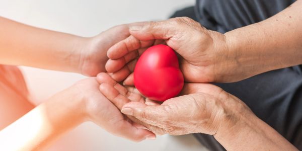 Two pairs of hands holding a red heart symbolizing care and compassion.