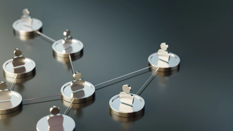 Metallic figures with an abstract human resources symbol connected by thin lines symbolising networking, teamwork, and relationships. The structure represents collaboration and communication within systems, emphasising connection within an abstract framework.