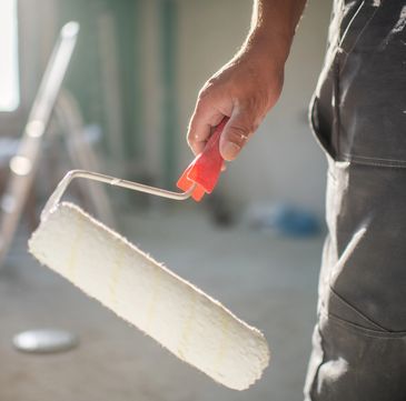 Person holding a paint roller covered in white paint.