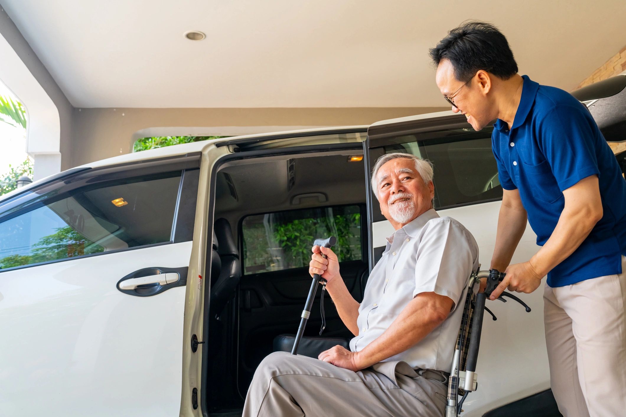 Caregiver helping elderly man in wheelchair into a vehicle.