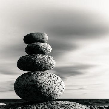 Stack of smooth stones balanced on each other against a cloudy sky.