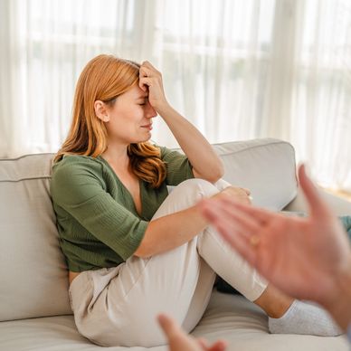 Woman appears stressed or upset, sitting on a couch with her hand on her forehead.