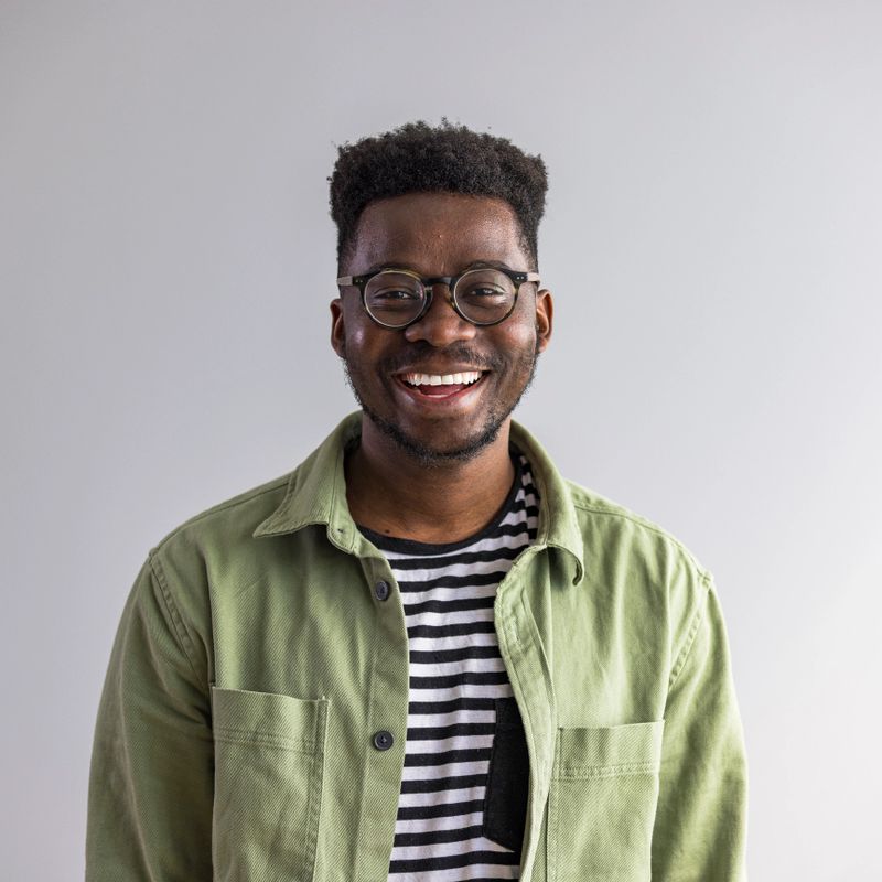 Brightly smiling man wearing glasses and a casual outfit, radiating joy and positive energy, captured against a minimalist neutral background.