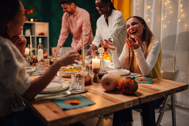 Cheerful friends laughing and sharing stories while enjoying a festive thanksgiving dinner together in a warm, cozy home atmosphere