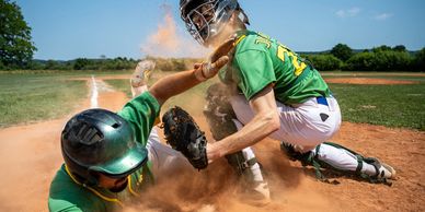 Baseball players in action with dust flying during a play at home plate.