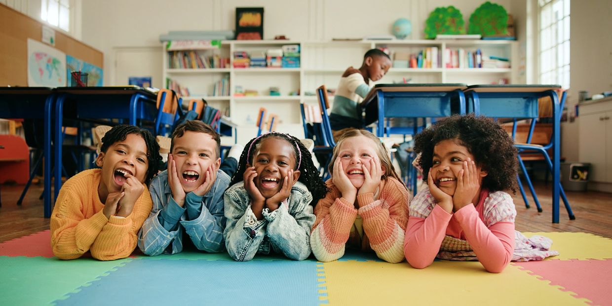 Five kids lying on the floor smiling in a classroom.