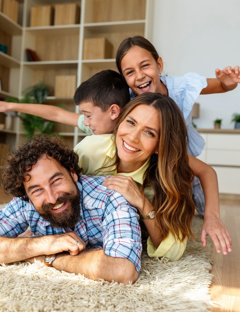 Two children and their parents are playfully lying on floor of cozy living room, smiling and embracing each other happily