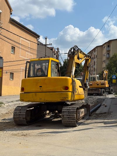 Two yellow excavators parked on a paved residential street.