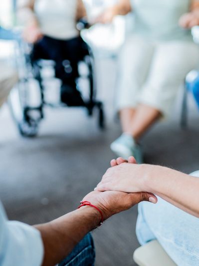 Two people holding hands in a supportive group setting.