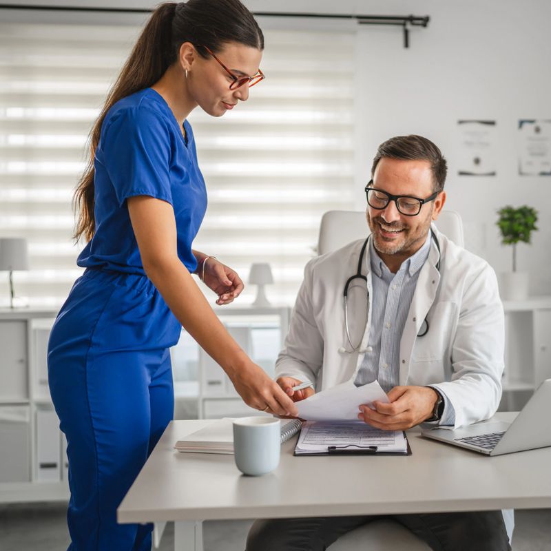 Male doctor and female nurse reviewing medical records at a desk in a christmas-decorated medical office, promoting collaboration and festive cheer