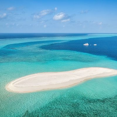 A small sandy island surrounded by clear turquoise waters under a blue sky.