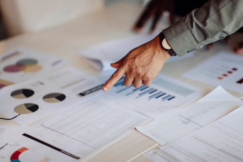 Hands pointing at charts and graphs on a table, reflecting collaboration, planning, and data-driven decision-making in a professional setting