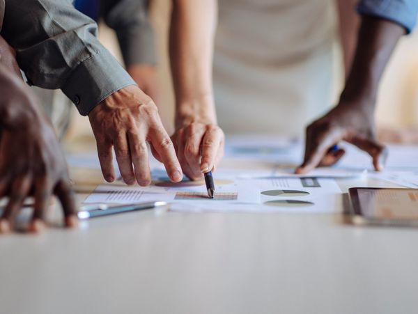 Hands pointing at charts and documents on a table during a meeting.
