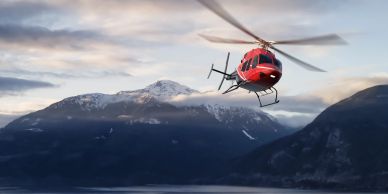 Red helicopter flying over snow-capped mountains.