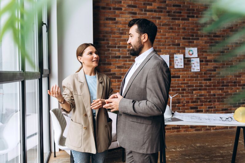 Two business partners are discussing a renewable energy project in a modern office, standing by the window and gesturing
