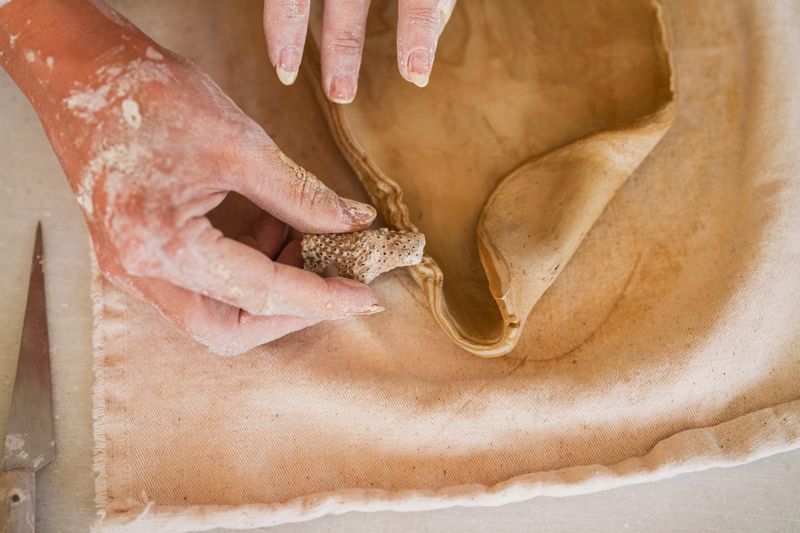 Close-up of artisan hands shaping and decorating the edge of a clay plate using a natural pumice stone in a pottery workshop. The creative technique highlights craftsmanship, handmade ceramics, and decorative detail in artisan production.