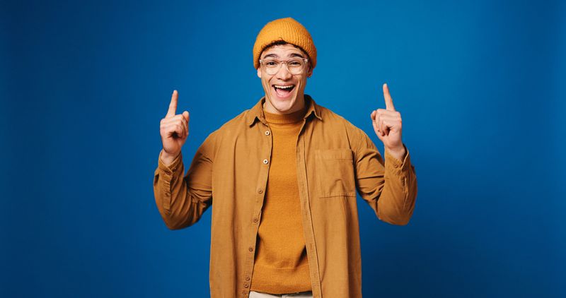 Portrait, man and pointing with smile in studio for advertising, announcement and coming soon. Excited, male person and hand gesture for sign up, promotion offer and giveaway guide on blue background
