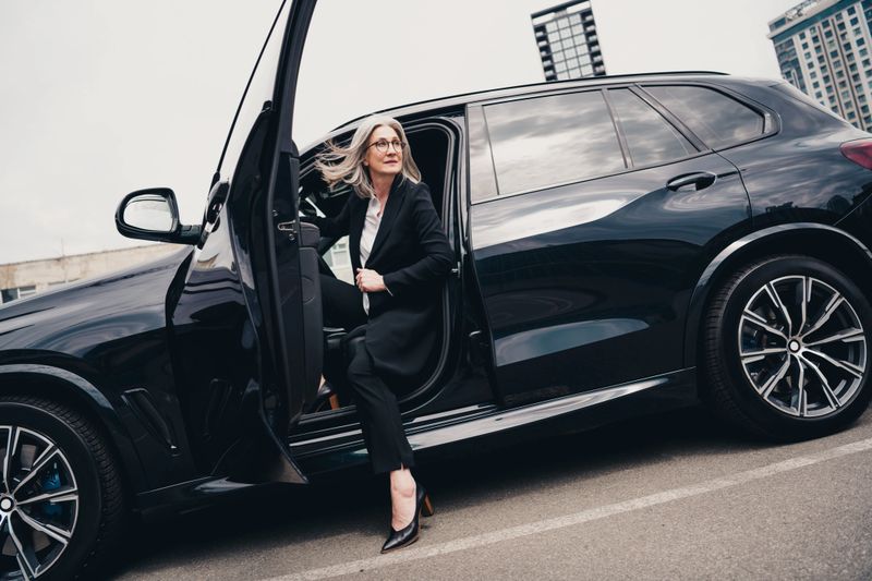 Elegant middle-aged professional woman stepping out of a luxury vehicle in the city, exuding confidence and sophistication.