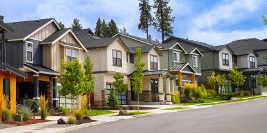 A row of modern suburban houses with trees and well-kept lawns.