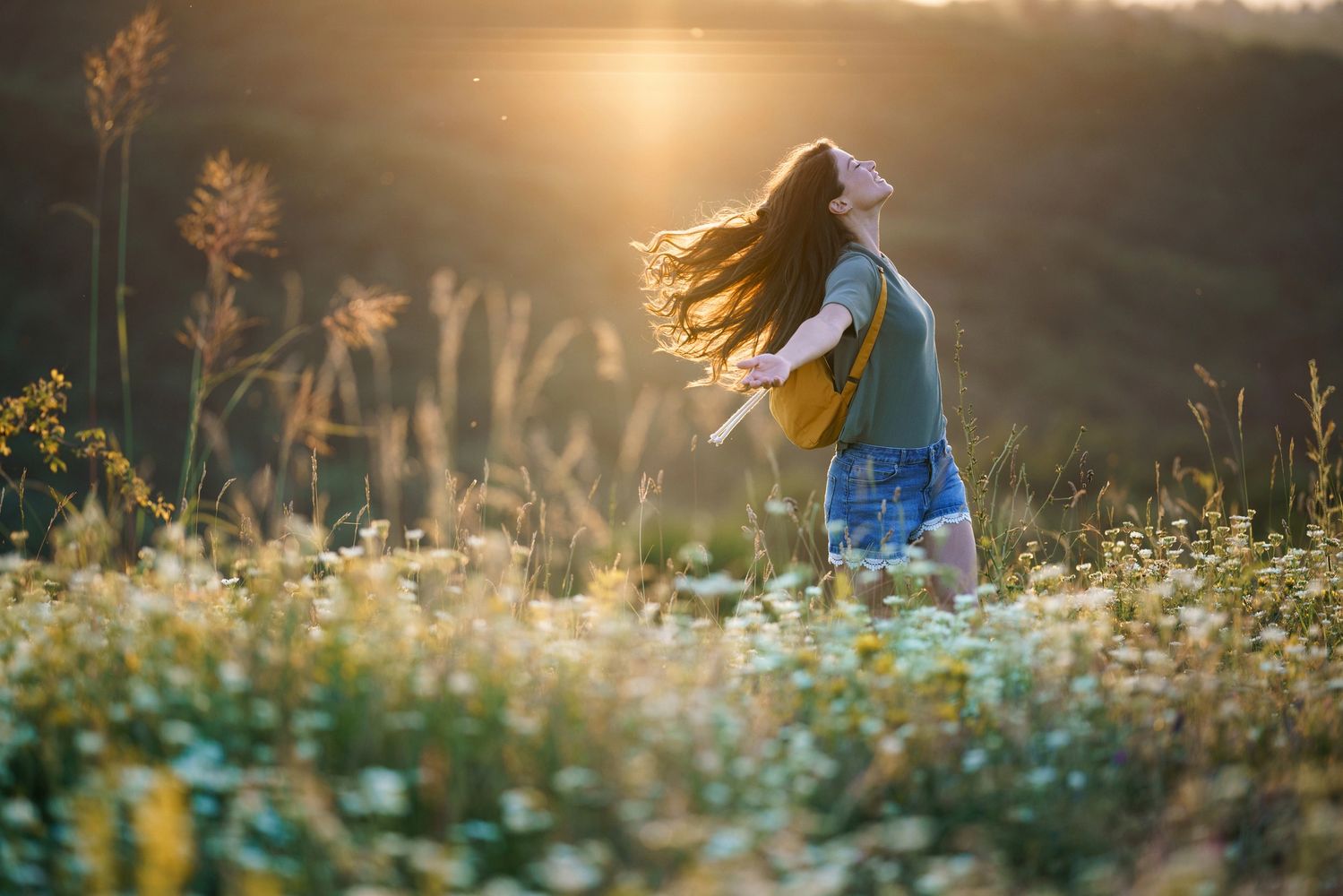 A woman stands on top of a mountain with her arms outstretched, breathing deeply, with flowers 